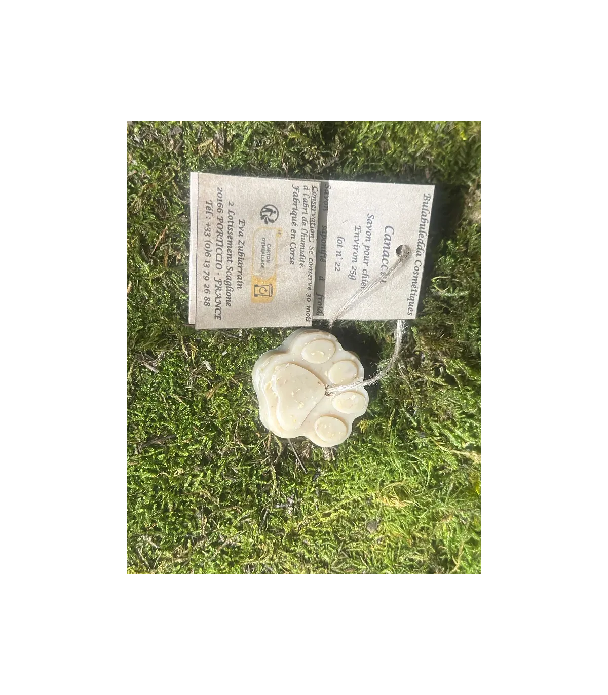 Savon Canacciu artisanal pour chien en forme de patte, devant ses étiquettes, posé sur de la mousse